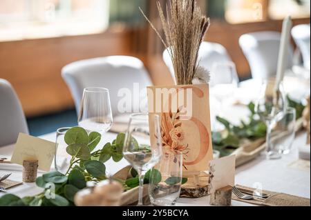 Decorazioni per matrimoni. Splendido luogo per eventi. Tavolo da ricevimento rotondo interno con fiori e sedie. Composizioni di fiori e piante in banchi di legno. Foto Stock