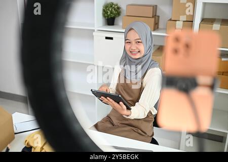 Giovane donna musulmana con hijab live streaming per vendere prodotti. E-commerce e concetto di piccole imprese Foto Stock