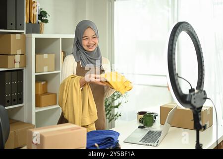 Giovane donna musulmana con hijab che lavora in diretta streaming per vendere prodotti. E-commerce e concetto di piccole imprese Foto Stock