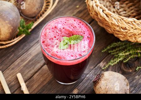Succo di barbabietola rossa in un bicchiere con foglie fresche di menta piperita su un tavolo, con cannucce di bambù Foto Stock