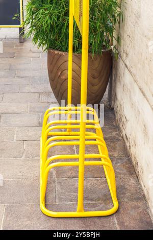Portabiciclette giallo brillante sul marciapiede urbano accanto a una grande piantatrice, concetto di infrastruttura urbana all'aperto Foto Stock