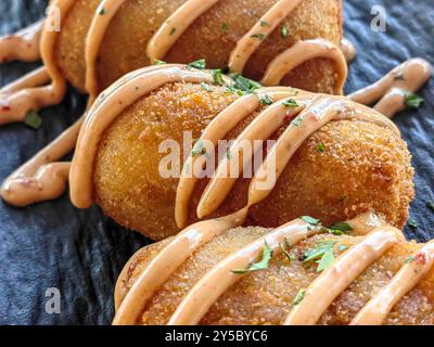 Primo piano di crocchette di patate con condimento e decorazione con prezzemolo, serviti in un piatto in ceramica nera. Foto Stock