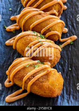 Antipasti con crocchette di patate serviti in un piatto in ceramica nera con condimento e decorazioni con prezzemolo Foto Stock