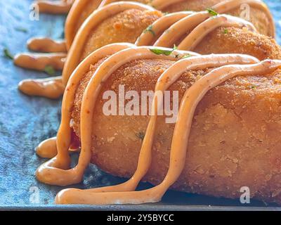 Primo piano di crocchette di patate con condimento e decorazione con prezzemolo, serviti in un piatto in ceramica nera. Foto Stock