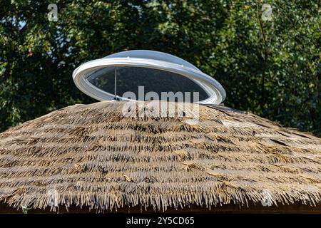 Apri la finestra rotonda sul tetto di paglia di una casa di villaggio Foto Stock