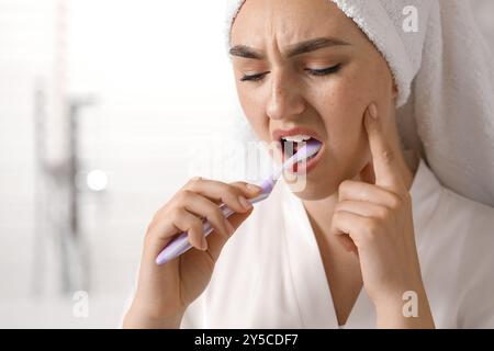 Giovane donna che soffre di mal di denti mentre si lava i denti in bagno Foto Stock