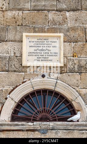 Colomba bianca seduta accanto alla finestra ad arco e alla targa commemorativa sopra la porta di Agios Nikolaos di Molos in piazza Solomos sull'isola di Zante Foto Stock