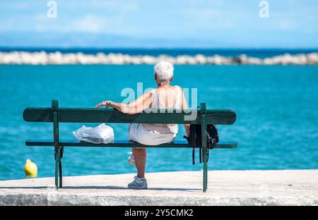 donna matura più anziana, donna seduta su una panchina che guarda al mare nel profondo del pensiero, donna seduta da sola sulla panchina che sogna ad occhi aperti, donna matura sulla panchina da sola. Foto Stock