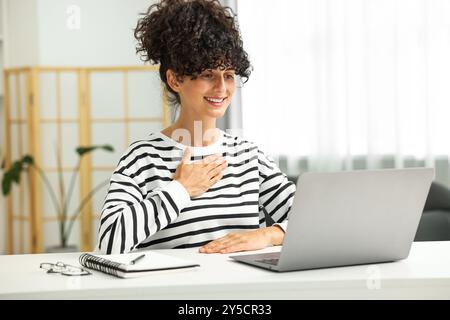 Giovane donna che usa il linguaggio dei segni per comunicare durante una videochiamata al tavolo bianco in interni Foto Stock