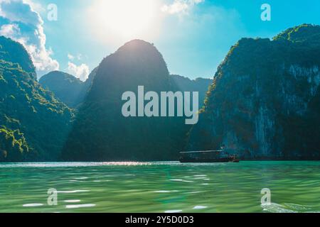 Tradizionale barca da pesca vietnamita che naviga nella baia di ha Long con i raggi del sole sulle acque blu incontaminate tra le montagne. Il paesaggio da sogno delle une di ha Long Bay Foto Stock