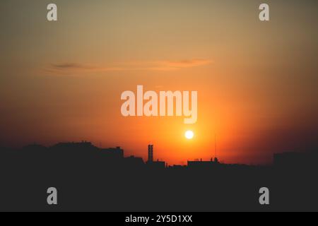 Il sole nascente proietta un bagliore luminoso sulla silhouette della città, trasformando il cielo in un bellissimo arancione. Foto Stock