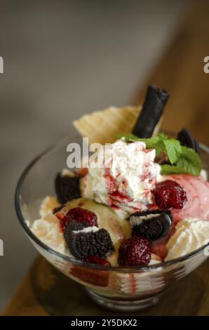 Dessert con gelato al lampone e al pistacchio in una ciotola di vetro con biscotti al cioccolato e frutti di bosco Foto Stock