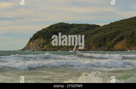 Uomo con windsurf affronta le onde al tramonto nel Golfo di Baratti, Piombino, Livorno, Italia Foto Stock