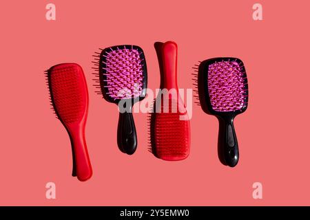 set di varie spazzole per capelli in plastica disposte in modo ordinato su uno sfondo rosa tenue, vista dall'alto. I pennelli presentano una varietà di forme, dimensioni e design Foto Stock