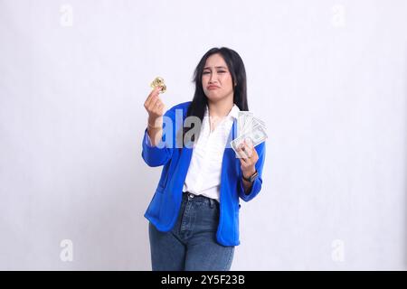 Elegante donna d'ufficio adulta che indossa una tuta formale blu in piedi che piange davanti alla macchina fotografica con dollaro e bitcoin sullo sfondo bianco isolato. per trasf Foto Stock