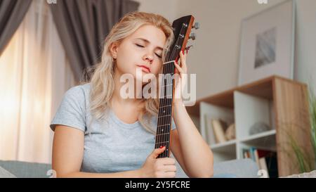 Musa perduta. Donna sconvolta. Chitarra. Una donna triste da sogno che tiene in mano uno strumento musicale e che sente un romantico dolore seduto, luce interna della stanza. Foto Stock