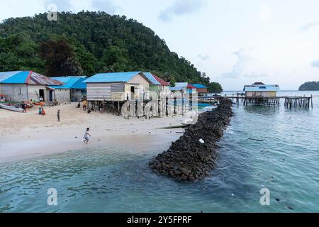 Bambini locali che giocano su una spiaggia vicino al mare nel villaggio popolare di Bajau a Labengki, Sulawesi, Indonesia, circondato da case su palafitte Foto Stock