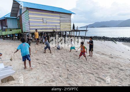 Bambini locali che giocano su una spiaggia vicino al mare nel villaggio popolare di Bajau a Labengki, Sulawesi, Indonesia, circondato da case su palafitte Foto Stock