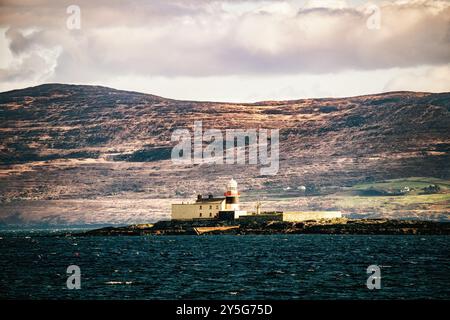 Le colline ondulate formano uno sfondo suggestivo per il faro. Nuvole scure si stagliano sul paesaggio montuoso. Foto Stock