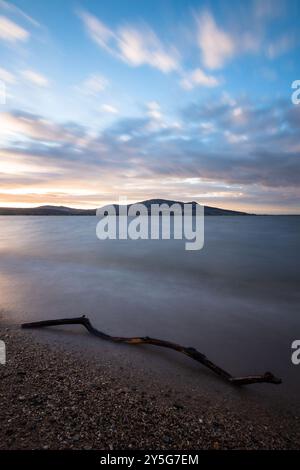Paesaggio a lunga esposizione al tramonto - il sole sta tramontando all'orizzonte, le nuvole nel cielo blu si muovono, l'acqua della diga come velluto, l'ultima Foto Stock