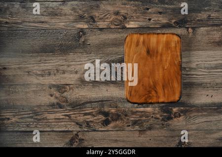 Un tagliere in legno splendidamente lavorato è collocato su un tavolo in legno rustico, che mostra i suoi grani naturali e i toni caldi. L'impostazione evoca un sens Foto Stock