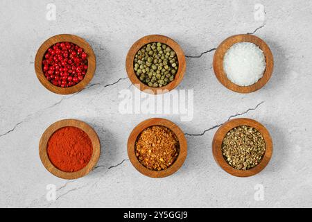 Spezie colorate e condimenti sono ordinatamente disposti in ciotole di legno su una superficie ruvida, mostrando vari sapori come grani di pepe, paprika e ch Foto Stock