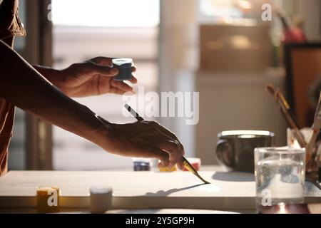 Pennello da lavoro luminoso con varie forniture artistiche sparse sulla scrivania. La luce del sole che scorre attraverso la finestra crea un'atmosfera calda in un ambiente creativo Foto Stock