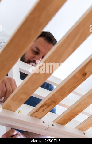 Un uomo sta lavorando su un telaio di legno. È concentrato sul compito che sta svolgendo ed è di umore serio Foto Stock