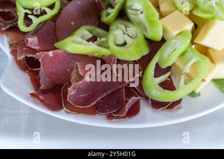 Selezione di salumi con formaggio giallo e peperoni verdi – antipasti in piatto. Foto Stock