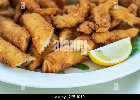 Bastoncini di pollo, Nuggets e bocconcini di prosciutto: Delizie fritte con limone e lattuga, servite su piatto bianco. Foto Stock