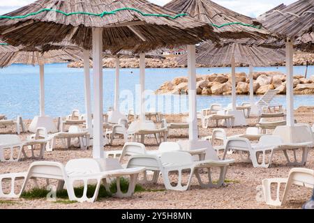 Tribunj, Croazia - 14 settembre 2024: Ombrelloni e lettini in paglia pronti per l'affitto in concessione fronte mare , senza persone Foto Stock