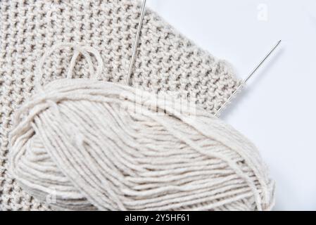 Palla grigia di fili per maglieria con aghi, un frammento di tessuto lavorato a maglia di un caldo maglione invernale, sciarpa o cappello, un hobby casalingo. Foto Stock