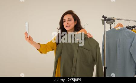 La blogger caucasica spensierata ragazza streamer sorridendo parlando filmando il blog influencer utilizza il telefono cellulare in studio. La modella felice donna confronta la moda dei vestiti Foto Stock