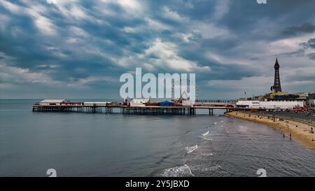 Una vista panoramica di un molo che si estende nel mare calmo, caratterizzato da una grande ruota panoramica e un'alta torre sullo sfondo. Il cielo è coperto di dramma Foto Stock