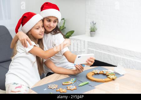 I bambini cucinano biscotti di Natale in un'accogliente cucina casalinga. I bambini adorabili nei cappelli di babbo natale preparano la cena per le vacanze in famiglia. Le sorelle preparano biscotti natalizi Foto Stock