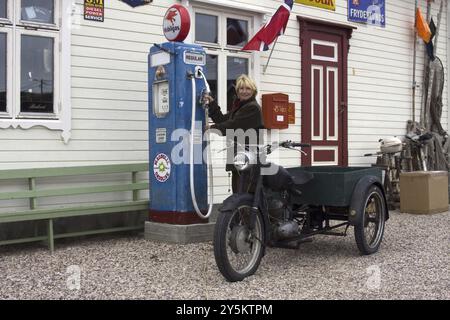 Donna bionda che fa rifornimento di benzina per la sua moto in una vecchia stazione di servizio, Kongsfjord, Varanger, Norvegia, Europa Foto Stock