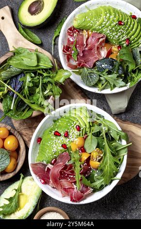 Bassa di un glucide ciotola. Insalata fresca verde con spinaci, rucola, avocado un prosciutto serrano in ciotola bianco e sfondo grigio, vista dall'alto Foto Stock