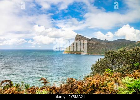 Splendida vista di un tranquillo paesaggio costiero caratterizzato da imponenti scogliere rocciose, lussureggianti fogliame e un mare blu calmo sotto un cielo parzialmente nuvoloso che fornisce un per Foto Stock