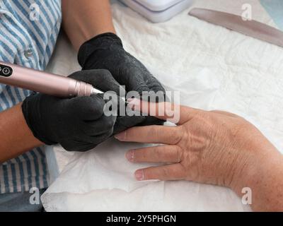 Un manicurista sta sta pulendo cuticole e residui di vernice dalle unghie di una donna con un trapano elettrico per unghie con bavatura a fiamma Foto Stock