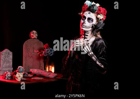 Donna con rosa nera che partecipa alla festa dia de los Muertos, preservando le tradizioni culturali tra generazioni. Donna inquietante con fiori che indossa il costume la Catrina per celebrare la cultura messicana Foto Stock