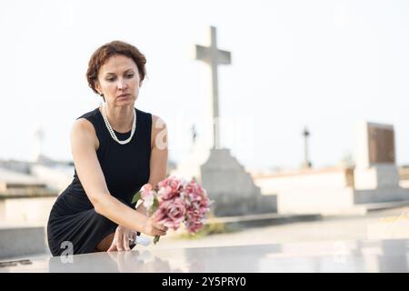 Donna addolorata in nero che mette il bouquet sulla tomba Foto Stock