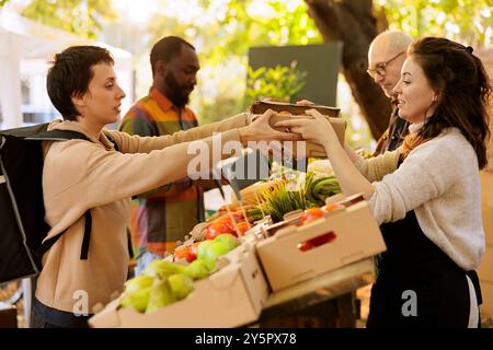 Agricoltore donna che consegna una scatola di frutta e verdura biologica naturale al corriere donna, offrendo ai clienti cibi sani coltivati localmente. Addetto alla consegna che accetta gli ordini per i clienti. Foto Stock