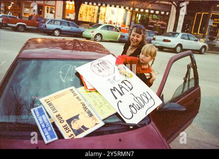 Una donna e un bambino preparano i cartelli di protesta contro la guerra a Bloomington, Indiana, durante le proteste del 2003 contro la guerra in Iraq. I segni, tra cui uno che recita "Stop the Mad Cowboy", riflettono la diffusa opposizione al conflitto, mentre i manifestanti si unirono per esprimere le loro preoccupazioni contro George W. Bush Foto Stock