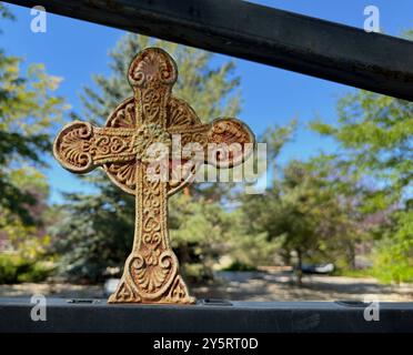 Una vecchia croce di ferro decora una recinzione nel giardino commemorativo della chiesa episcopale a Cody, Wyoming. Patina, ruggine e un vecchio design artistico rappresentano la trinità. Foto Stock