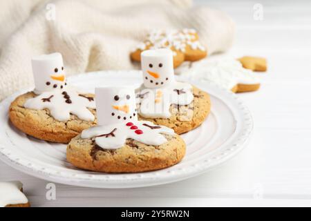 Deliziosi biscotti con pupazzi di neve fatti di marshmallow su tavola bianca, primo piano Foto Stock