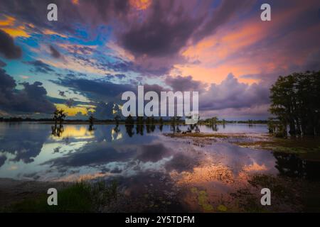 "Le tonalità dorate si riflettono sul tranquillo lago, mentre il sole scende sotto l'orizzonte, dipingendo il cielo in una sinfonia di colori." Foto Stock