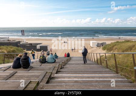 Egmond aan Zee, Paesi Bassi - 17 settembre 2024: Visitatori su gradini di legno verso una spiaggia sabbiosa dove alcuni si rilassano mentre altri passeggiano lungo la Foto Stock