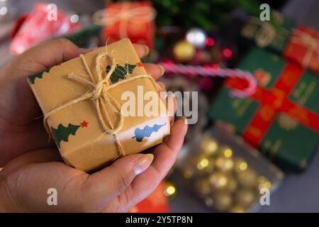 Mani femminili che reggono un piccolo regalo con sfondo sfocato di decorazioni natalizie durante il periodo natalizio Foto Stock