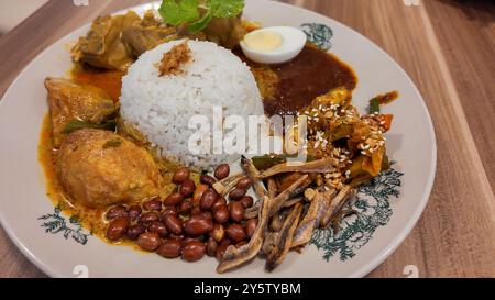 Cibo asiatico Nasi Lemak è un piatto di riso infuso con latte di cocco. Servito con sambal, pollo al curry, arachidi fritte, uova sode e acciughe fritte. Foto Stock