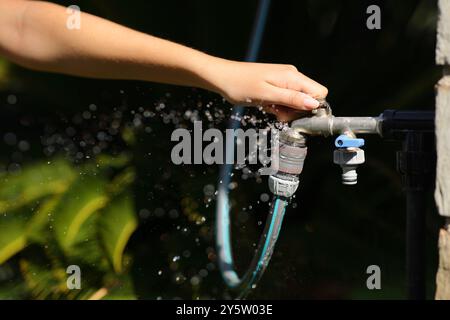 Primo piano di una donna che apra il rubinetto con una perdita d'acqua in giardino Foto Stock